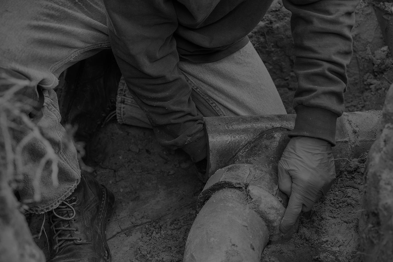 black & white picture of exposed sewage pipe with plumber's hand inside