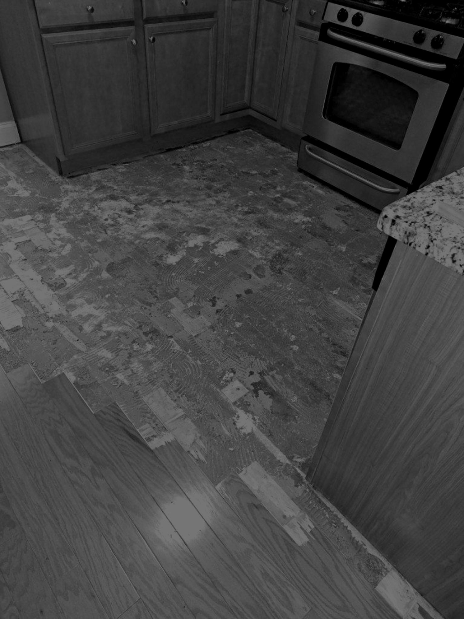 black & white picture of water damaged floor in kitchen after flooring has been taken up